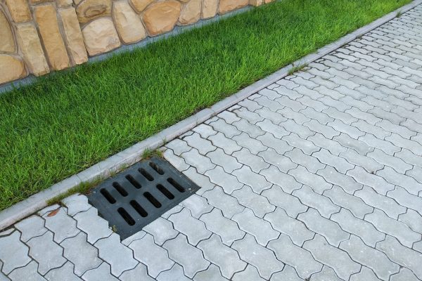 Plastic drain gutter, green grass lawn and stone pavement sidewalk.